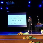 Kobieta z mikrofonem na scenie; w tle ekran z napisem podsumowującym dotychczasowe edycje Pól Nadziei