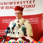 Rektor UwB ubrany w  togę mówiący do mikrofonów na tle napisu Uniwersytet w Białymstoku. 