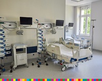 Sala szpitalna z pustymi łóżkami. Nad nimi na ścianach zawieszone są monitory