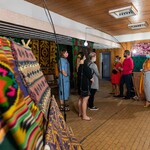 Sala wystawowa, na której prezentowane są tkaniny w etniczne wzory, grupa ludzi słucha wykładu 
