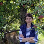 Kobieta stojąca pod jabłonią z której zwisają jabłka