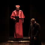 W świetle na scenie stoi aktor w stroju kardynała trzymając w ręku biblię. Po prawej klęczy aktor grający M. Sopoćkę