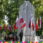 Pomnik ozdobiony biało-czerwonymi flagami oraz wieńcami. Na warcie stoi dwóch żołnierzy.  