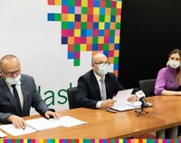 Na zdjęciu 3 widoczne osoby siedzące za stołem. W tle kolorowa grafika.