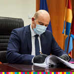 Marszałek Artur Kosicki w masce i rękawiczkach, podpisuje dokumenty siedząc przy biurku