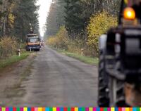Droga asfaltowa w lesie, na pierwszym i dalszym planie stoją dwie maszyny w trakcie budowy drogi