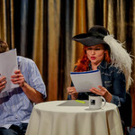 Przy stoliku nakrytym białym obrusem siedzi kobieta w kapeluszu i czyta. Obok siedzi mężczyzna zasłaniający twarz książką.