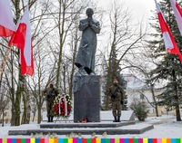 Na zdjęciu widoczny pomnik bł. ks. J. Popiełuszki i stojący żołnierze. Pod monumentem widoczne znicze oraz wieniec. Obok widoczne biało-czerwone flagi.