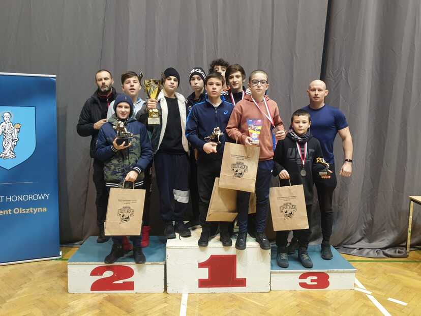 Grupa zawodników KS Wschód stojąca na podium wraz ze swoimi trenerami.
