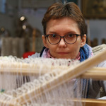 Kobieta w okularach patrząca w obiektyw trzymając głowe nad krosnami do tkania