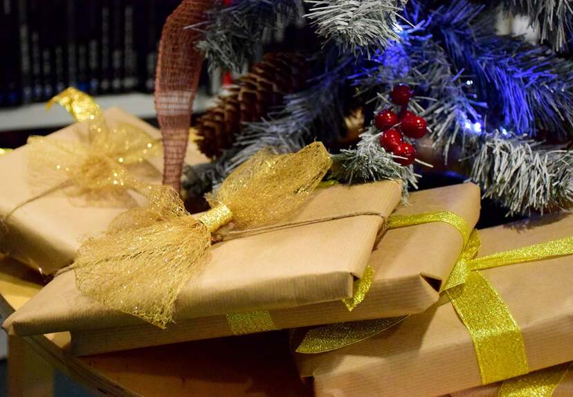 Zapakowane prezenty leżące pod choinką zawinięte w kokardy. W tle widoczne wiszące bombki na gałęziach