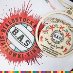 Logo BAS. Obok leży drewniana bombka z logo Białostockiej Akademii Siatkówki oraz życzeniami świątecznymi.