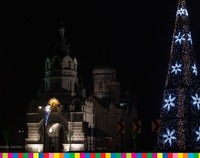 Po prawej choinka oświetlona lampkami w kształcie gwiazdek. Po lewej podświetlony kościół.
