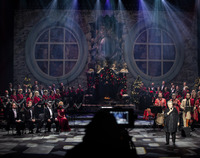 Muzycy na scenie przy instrumentach i mikrofonach. W tle scenografia: świąteczny kominek, po bokach okrągłe okna.