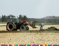 Rolnik pracujący na polu. Obok niego stojący traktor. W tle las.