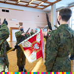 Na zdjęciu widoczni żołnierze z uniesioną do góry prawą dłonią. Stoją wokół sztandaru. W tle widoczni żołnierze ustawieni w szeregu