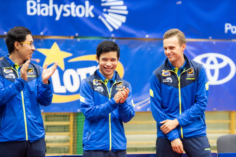 Na zdjęciu widoczni trzej zawodnicy tennisa stołowego w niebieskich kurtkach