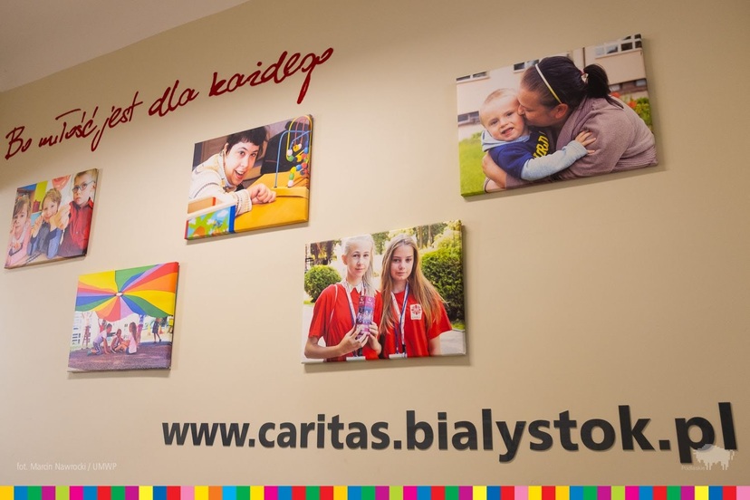 Ściana ze zdjęciami i stroną internetową Caritas