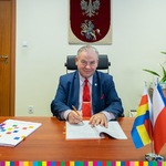 Wicemarszałek Marek Olbryś podpisuje umowę na wykonanie mikroinstalacji Wąsosz. Na biurku stoją flagi Województwa Podlaskiego oraz Polski