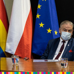 Wicemarszałek Marek Olbryś na tle flag: wojewódzkiej, biało-czerwonej i unijnej.