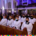 Mężczyźni ubrani w białe komże siedzą w ławkach w kościele