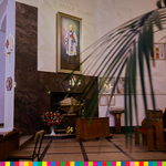 W oddali widoczny obraz z wizerunkiem kapłana. Z prawej storny wystają liście palmy