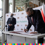 Wicepremier Piotr Gliński pochyla się nad stołem i podpisuje dokumenty.