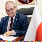 Marek Olbryś siedzi za biurkiem i podpisuje dokumenty 