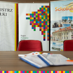 Za stołem stoją banery z logo Województwa Podlaskiego i Sokółki.