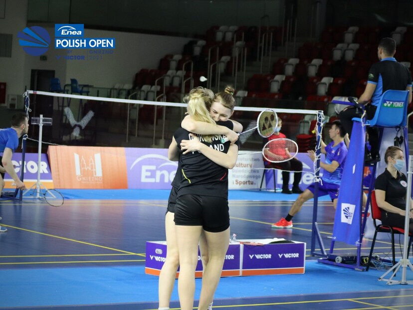 Zawodniczki badmintona przytulają się do siebie. W tle widoczna siatka oraz trybuny