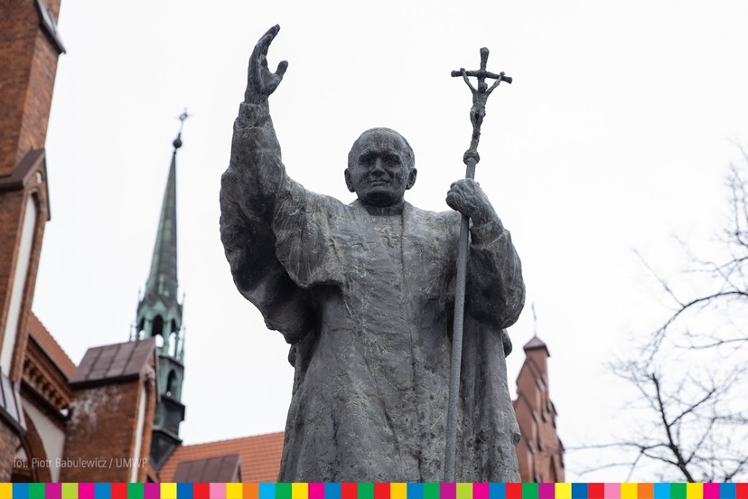 Pomnik, na którym papież podnosi prawą dłoń, w lewej trzyma krzyż.