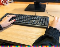 Dwoje rąk przy klawiaturze komputerowej.