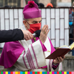 BP Henryk Ciereszko w masce czyta modlitwę z księgi. Wznosi dłoń w geście błogosławieństwa