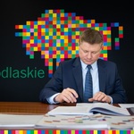 Mężczyzna w graniturze podpisuje dokumenty. W tle żubr zrobiony z kwadratowych kolorowych pikseli