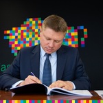 Mężczyzna w graniturze podpisuje dokumenty. W tle żubr zrobiony z kwadratowych kolorowych pikseli