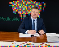Marek Malinowski podpisuje dokumenty. Za nim czarna ścinaka z logo Województwa Podlaskiego