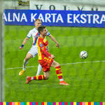 Przez siatkę bramki widać dwóch piłkarzy. Obok nich lecąca piłka