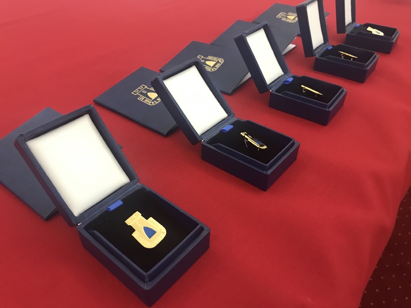 Złote odznaki „Za opiekę nad zabytkami” w pudełkach ozdobnych leżą na czerwonym materiale