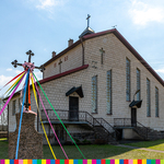 Kościół z cegieł. Przed kościołem znajduje się krzyż z kolorowymi wstążeczkami