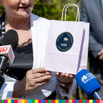 Wiesława Burnos, członek zarządu województwa podlaskiego stoi przed mikrofonami i trzyma papierową torebkę.