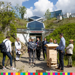 Grupa osób stojąca przed Uniwersyteckim Centrum Przyrodniczym podczas konferencji prasowej. Obok nich stoi drewniany ul.