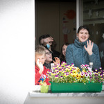 Dzieci stojące przy otwartym oknie machają osobie robiącej zdjęcie