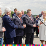 Osoby uczestniczące w wydarzeniu otwarcia mostu stoją przed mikrofonami. Wsród nich znajduje się Członek Zarządu Województwa Podlaskiego, Wiesława Burnos.