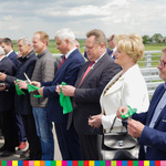 Osoby uczestniczące w wydarzeniu otwarcia mostu przecinają zieloną wstęgę. Wsród nich znajduje się Członek Zarządu Województwa Podlaskiego, Wiesława Burnos.