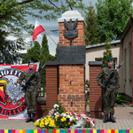 Dwóch żołnierzy stojących przy pomniku pod krórym leżą kwiaty