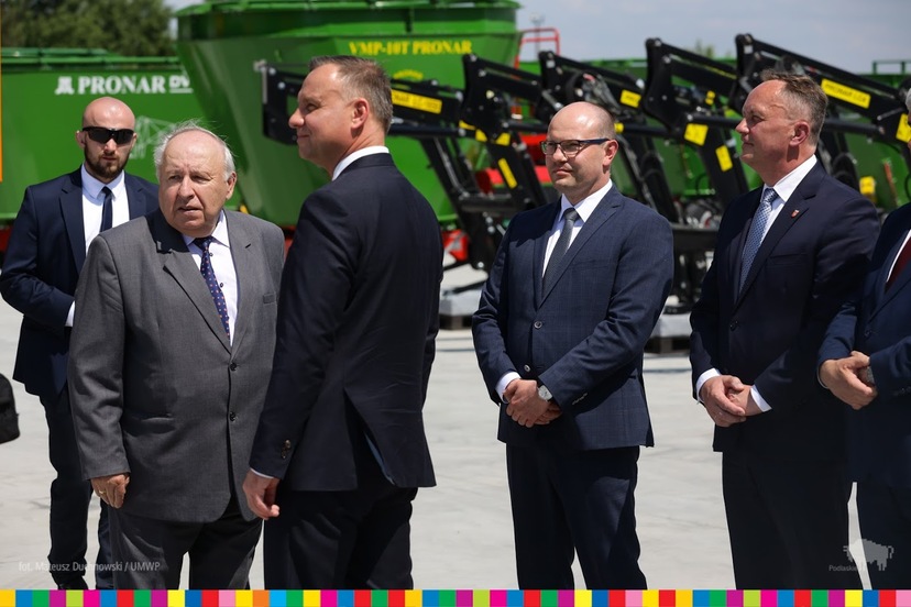 Na zdjęciu stoi pięciu mężczyzn w garniturach na tle maszyn rolniczych, w tym marszałek Artur Kosicki