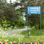 Tablica z napisem Gmina Suraż Wita stojąca przy drodze wiodącej przez las