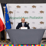Marszałek Kosicki za stołem. Obok flaga Polsi i UE, w tle ścianka z logotypami woj. podlaskiego
