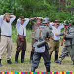 Mężczyźni poprzebierani w niemieckie mundury z czasów drugiej wojny światowej mierzą bronią do mężczyzn przebranych za partyzantów z uniesionymi rękoma za głowę