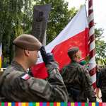 Żołnierze pod pomnikiem, jeden z nich wciąga flagę na maszt